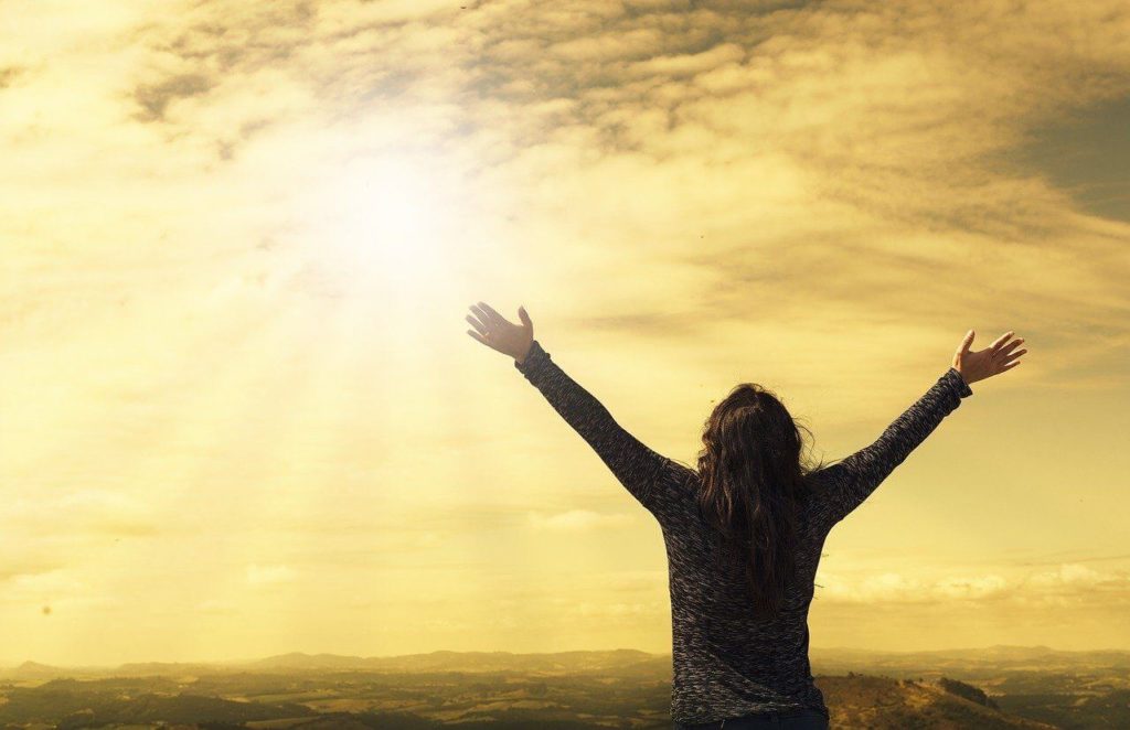 女性が太陽に向かって両手を上げている画像